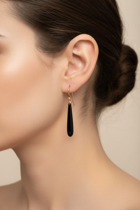 Close-up of a woman wearing a black teardrop earring with a neutral background