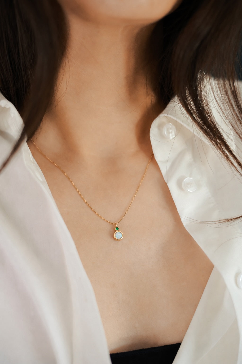 Round two stone necklace with opal main stone and diamond accent in gold on model with shirt