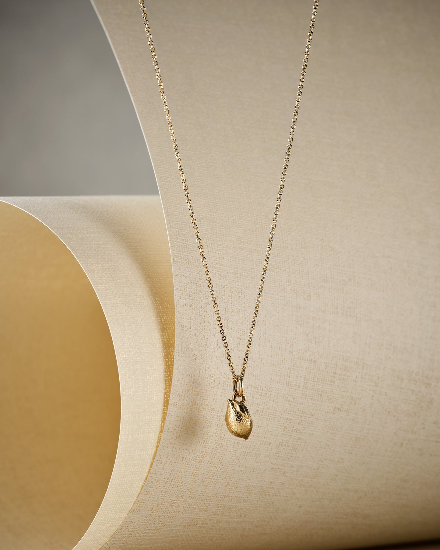 tiny gold lemon necklace on beige background