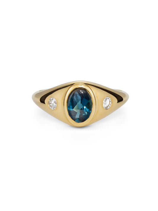A yellow gold signet-style ring featuring a central oval-cut London blue topaz and two small round diamonds on either side.