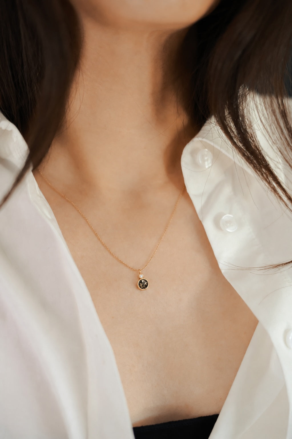 Two stone gold necklace with black and gold stone and white diamond on a model with open shirt