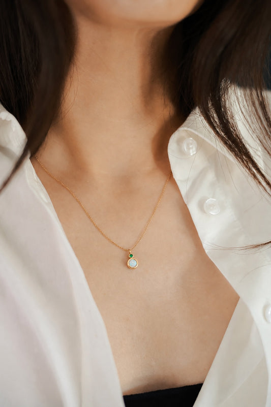 Round two stone necklace with opal main stone and diamond accent in gold on model with shirt