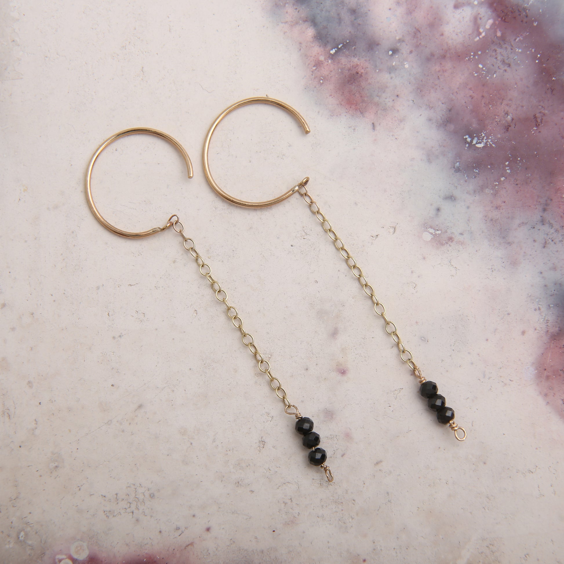 gold hoop earrings with gold chain and black spinel gemstones - pink marbled background