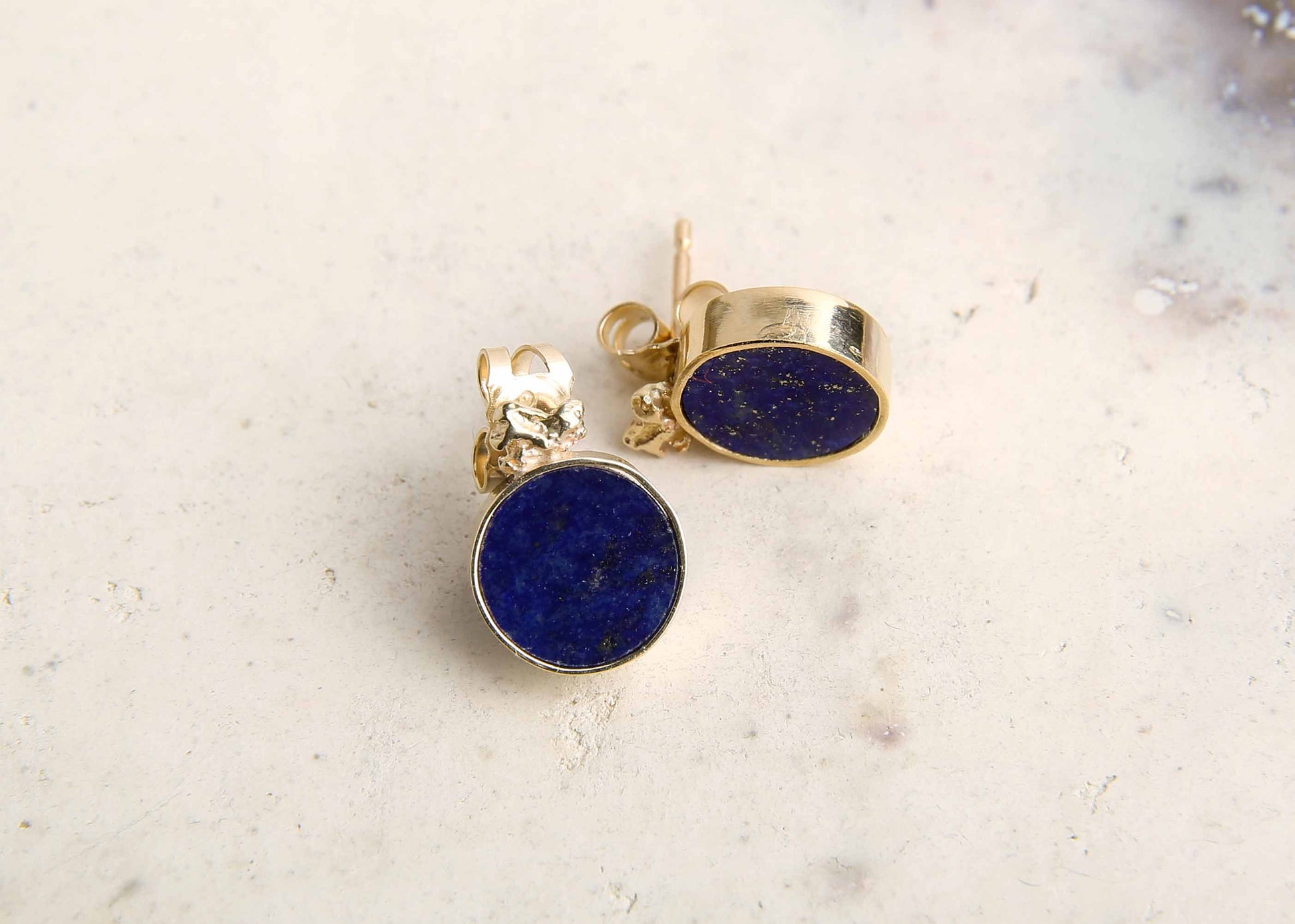 Blue lapis lazuli and gold disc stud earrings on pink marble table