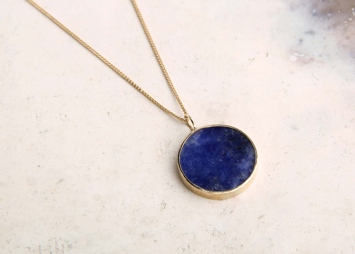 Blue lapis lazuli and gold pendant necklace on pink marble