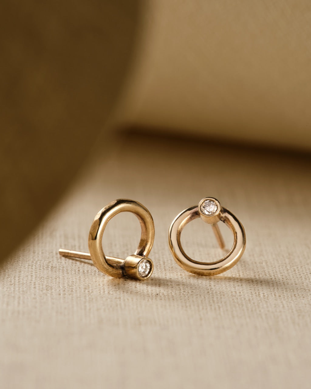 close up of diamond and gold circle stud earrings on beige background