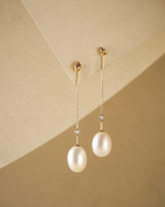 drop stem gold earrings with pearl and diamonds beige background