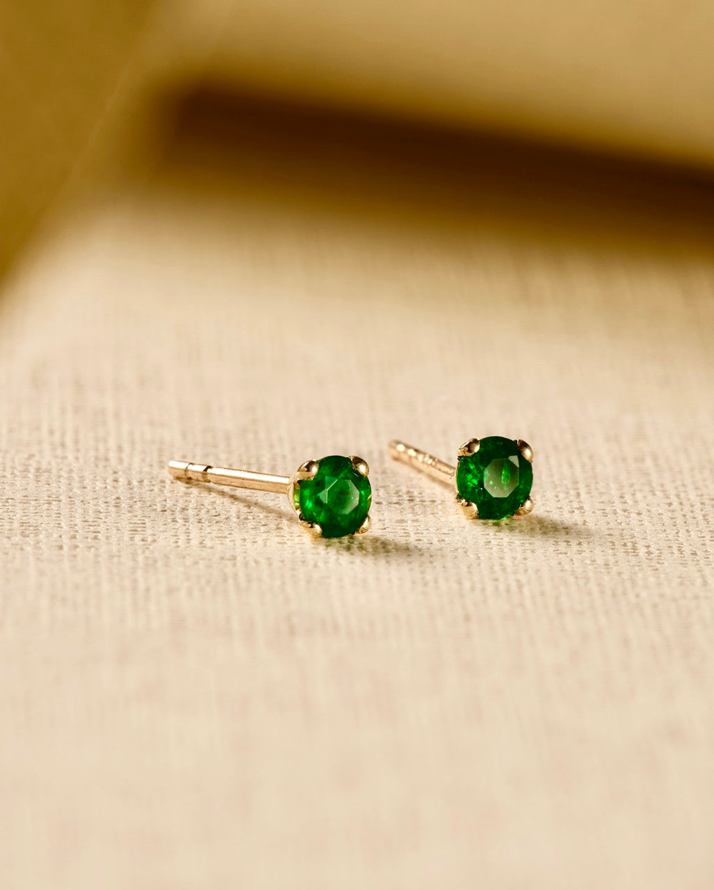 Emerald gold stud earrings on beige material