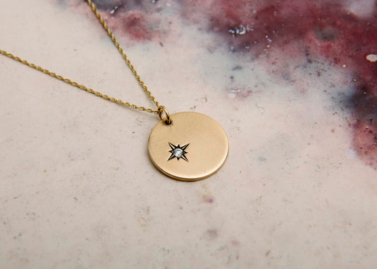 handmade gold disc pendant necklace with star set diamond on pink marbled background