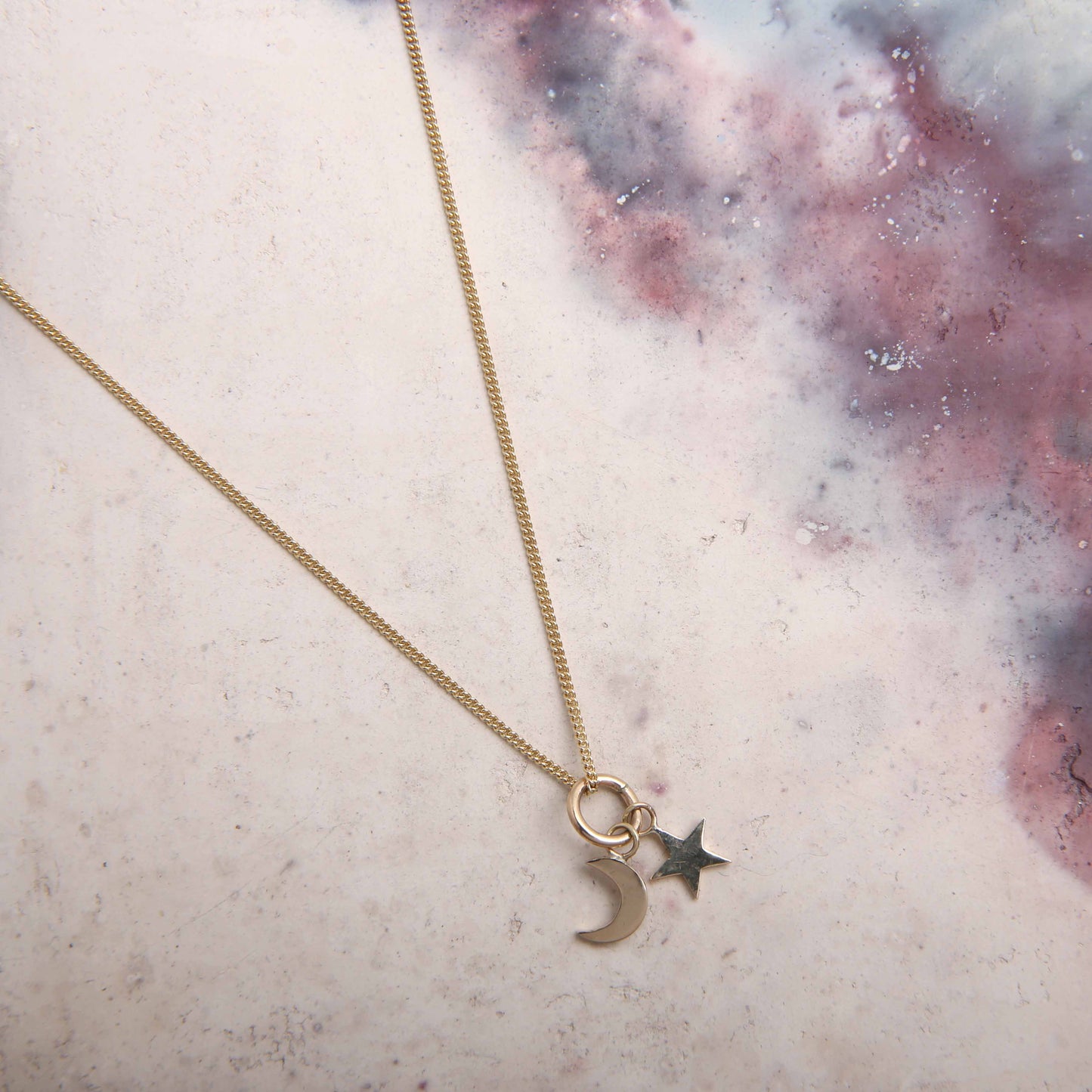 handmade gold moon and star pendant necklace on pink marbled background