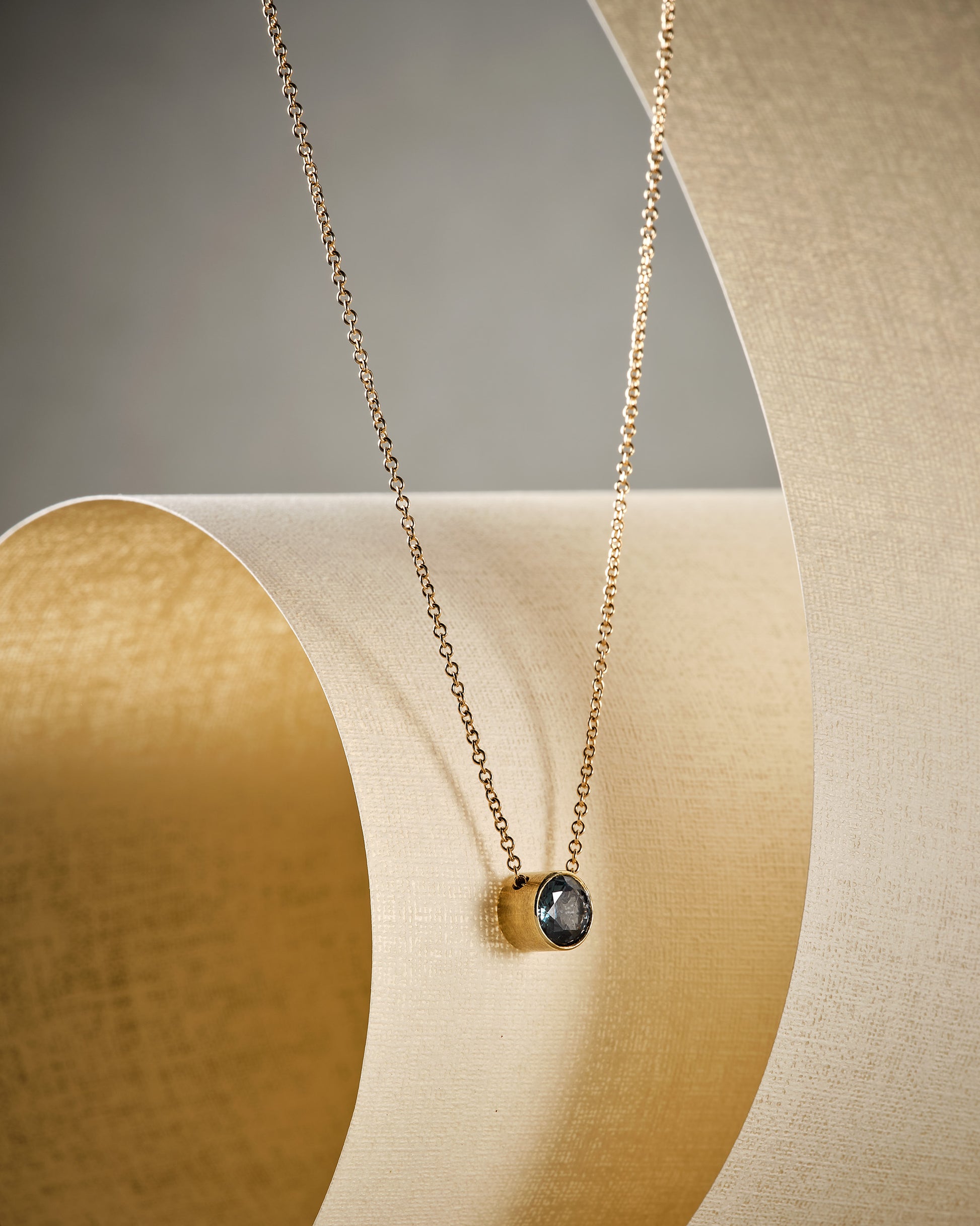 modern, classic delicate blue grey spinel gold necklace on beige material with shadow